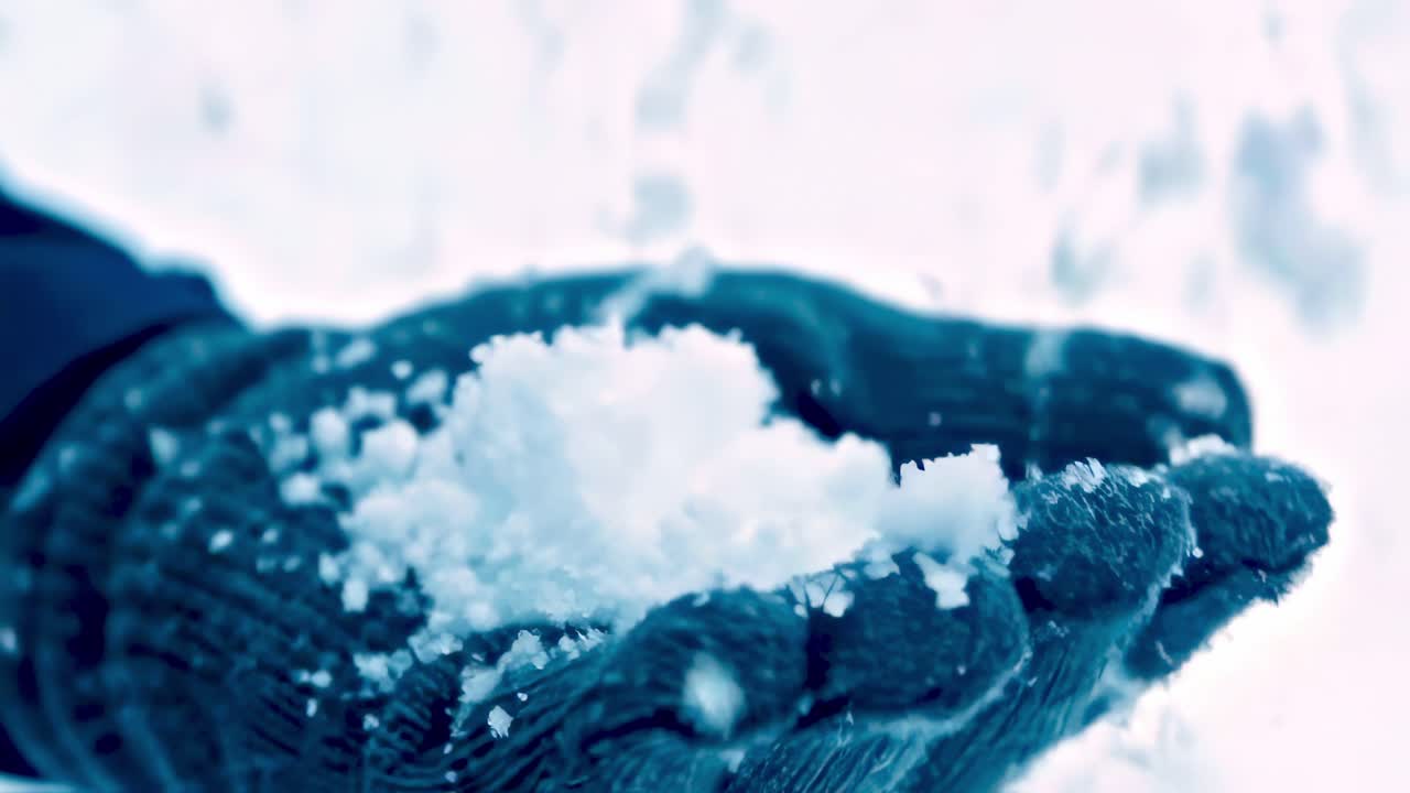 Snowflakes gently falling on gloved hands grasping freshly gathered snow, capturing winter's delicate and peaceful landscape moment