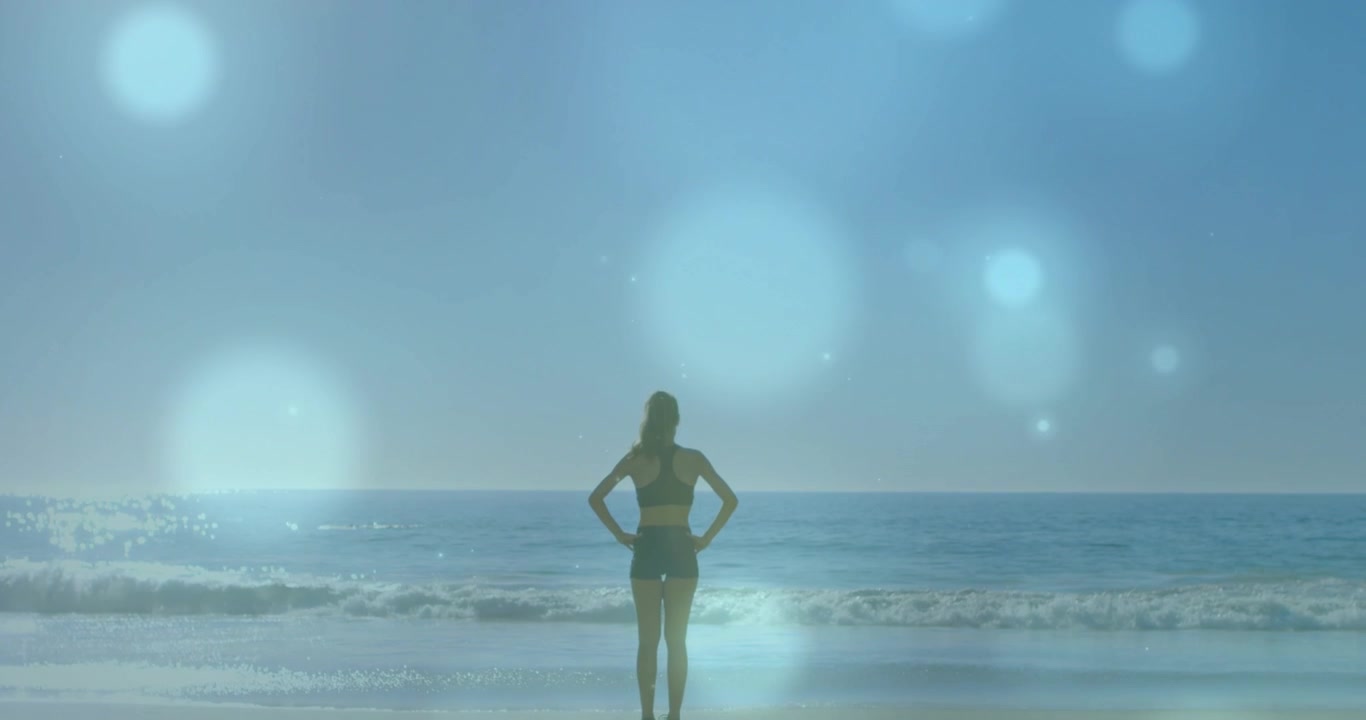 Donna in piedi con le mani sui fianchi sulla riva, la telecamera si avvicina con sfere luminose sovrapposte, allenamento fitness