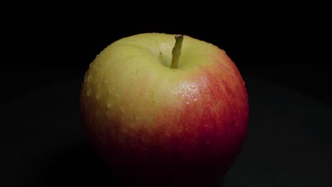 manzana con gotas de agua sobre fondo negro, primer plano inclinado hacia abajo