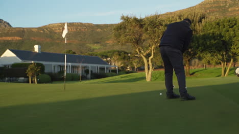 golfista tomando putt en el putting green al amanecer con montañas en el fondo