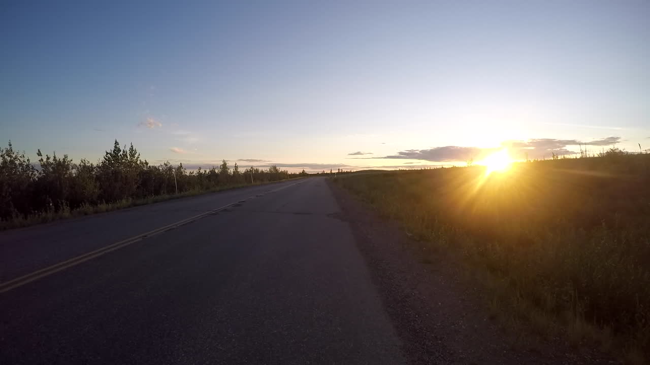 conduciendo hacia la puesta de sol en alaska en un camino lleno de baches