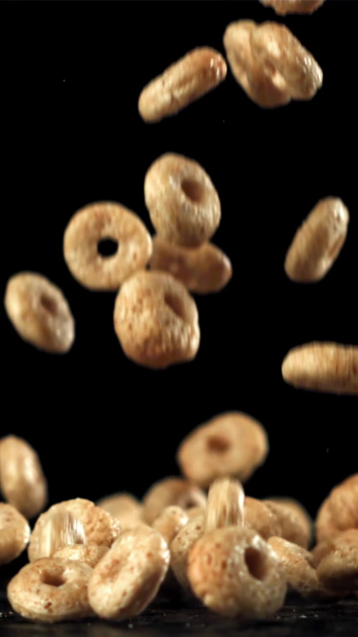 Anelli di cereali dorati che cadono al rallentatore su sfondo nero