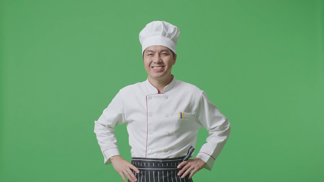 Asian Man Chef With Arms Akimbo Looking At Camera And Smiling While Standing In The Green Screen Background Studio