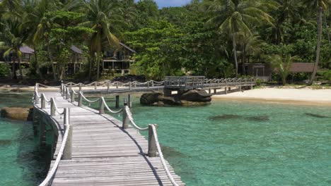 puente de madera que conduce a una isla tropical de playa de arena blanca.