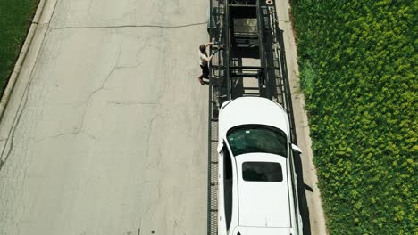 pickup-truck-driver-car-hauler-securing-cars-with-straps-on-trailer-drone-footage-4k