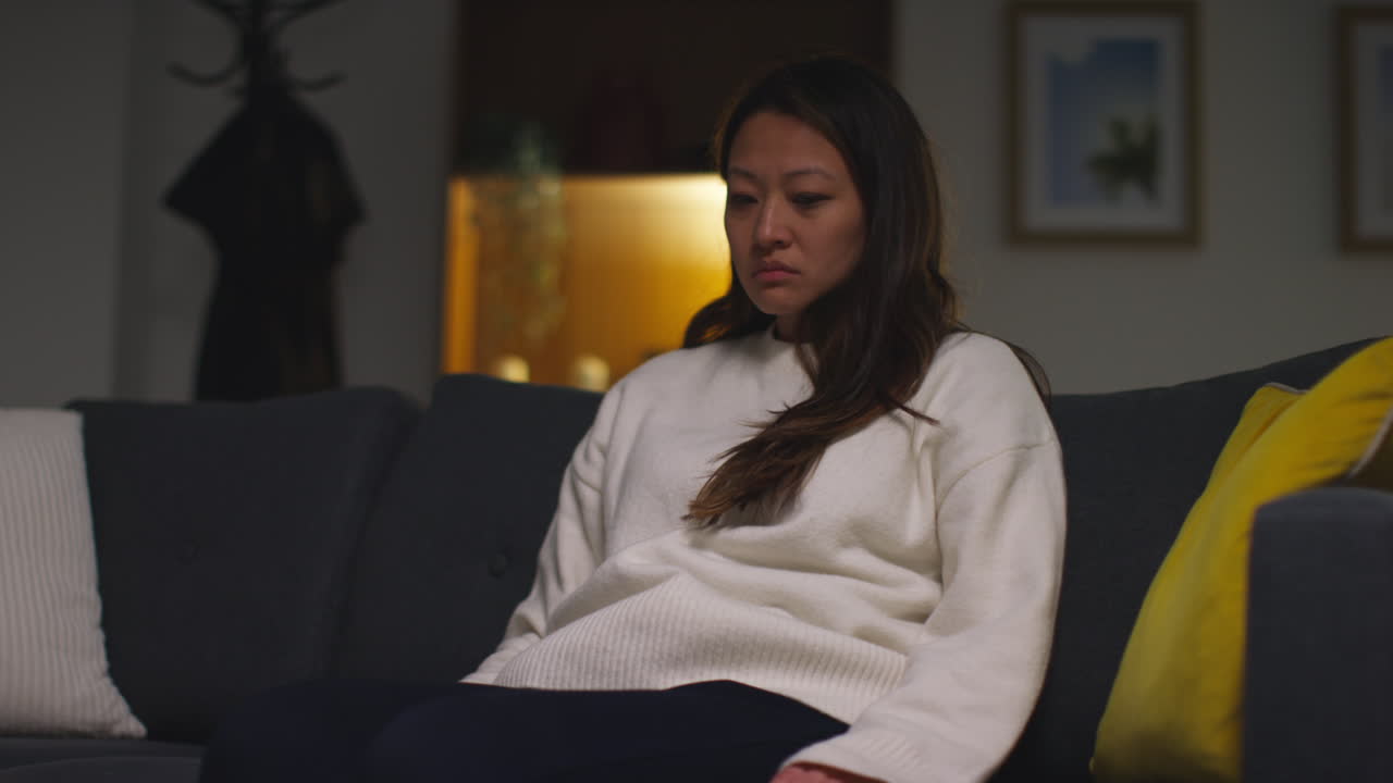 Stressed Or Anxious Woman Suffering With Depression Anxiety Or Loneliness Sitting On Sofa At Home In The Evening