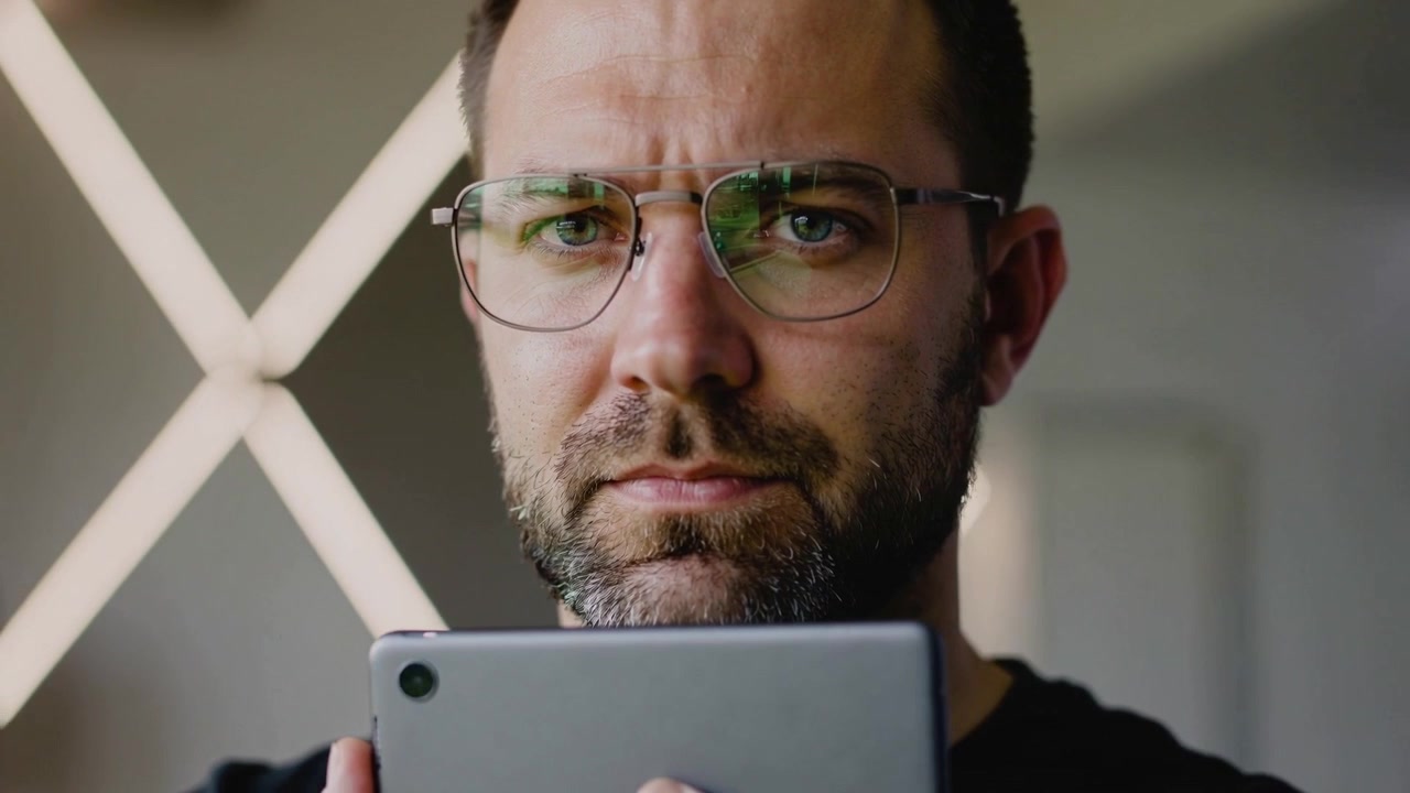 Camera pulling in, man holding gray tablet checking framing and LED glow on glasses in studio
