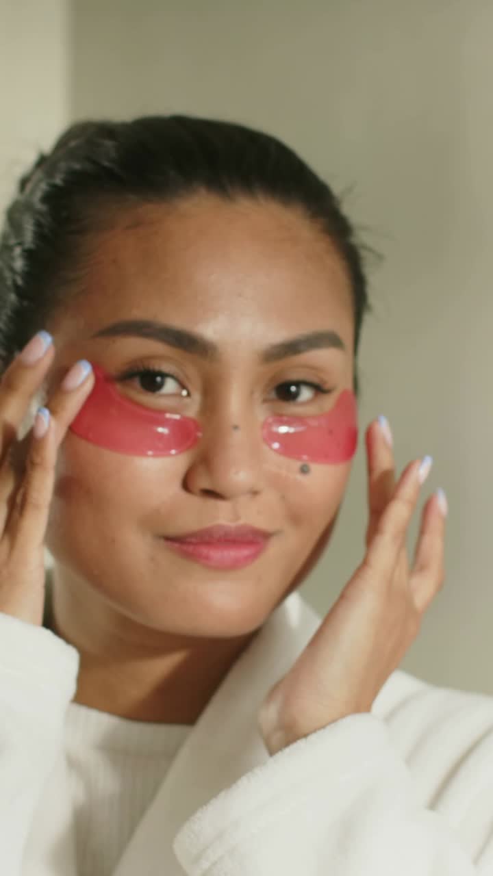 Vertical video: Recording midadult Asian woman rubbing red patches at home spreading gel, in robe