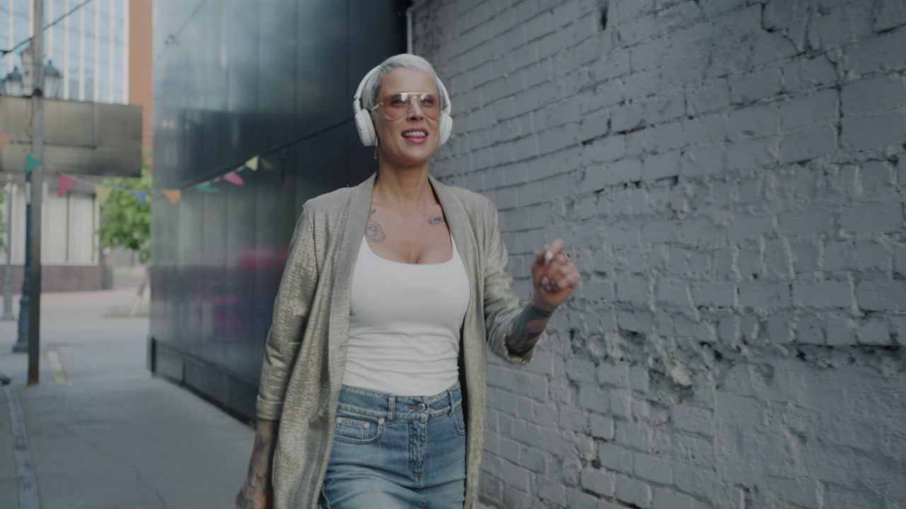 Stylish Woman Dancing and Listening to Music in a City Alley