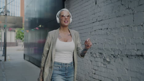 stylish woman dancing and listening to music in a city alley