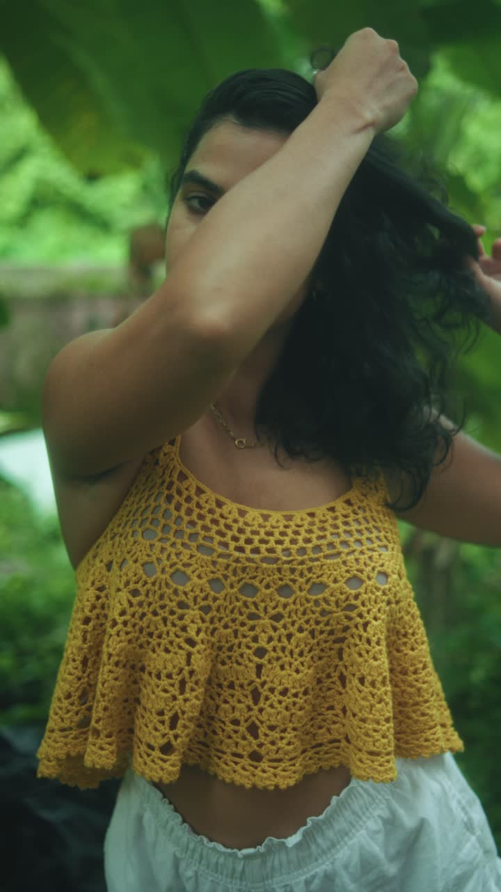Woman in yellow top posing outdoors with foliage, relaxed mood