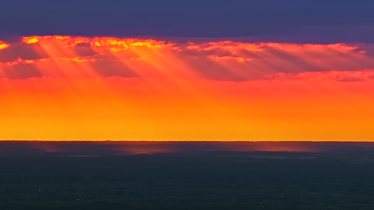 Dramatic sunset timelapse with golden beams pouring through a break in dark clouds, illuminating the distant landscape with warm, glowing light