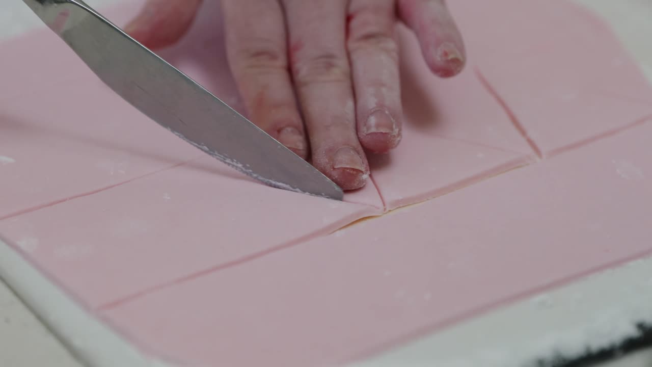 A person cuts triangles into pink fondant icing with a butter knife using her hands and fingers to hold icing in place