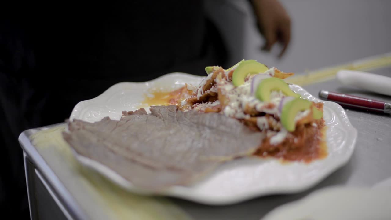 Chef sou-chef cook preparing a traditional mexican dish called chilaquiles adding a piece of roasted salted meat called cecina at a local cafe diner restaurant in latin america