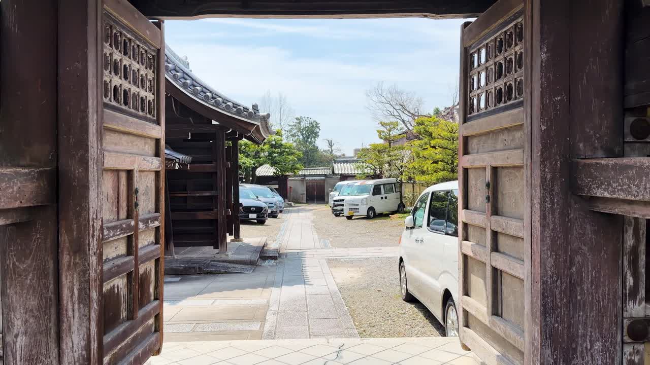 カメラが日中の光の下、歴史ある木製の門を通り抜け、伝統的な日本の寺院の境内へと移動する