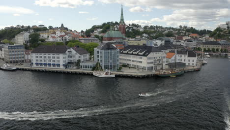 speedboats sailing and leaving a wake on the norwegian coast near the pollen harbor, clarion hotel and trinity church in tyholmen, arendal, norway