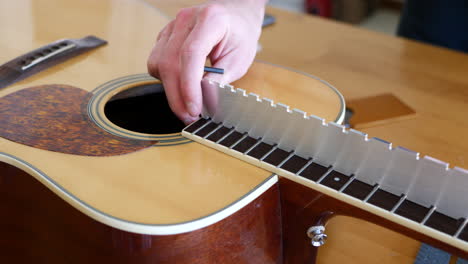 Close-up-hands-of-a-luthier-craftsman-adjusting-and-leveling-the-trussrod-of-an-acoustic-guitar-neck-fretboard-on-a-wood-workshop-bench-with-lutherie-tools