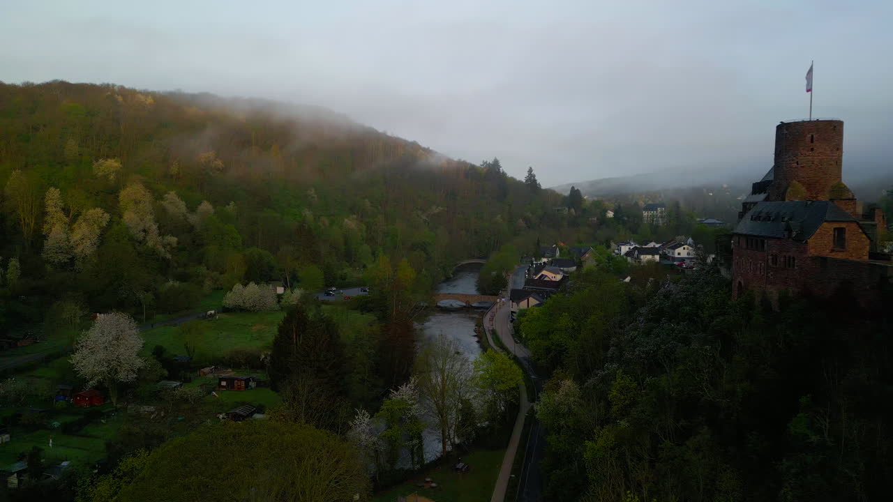 Vorbeiflug am auf einem Hügel gelegenen Schloss Hengebach entlang der Rur an einem nebligen Morgen in Heimbach, Deutschland. - Luftaufnahme