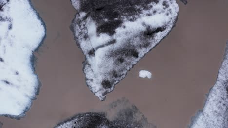 frozen icebergs with black ash on surface floating in brown glacial lagoon water