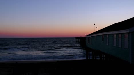 clear sky at sunrise in the outer banks of north carolina as waves roll onto the sand beside a wooden fishing pier