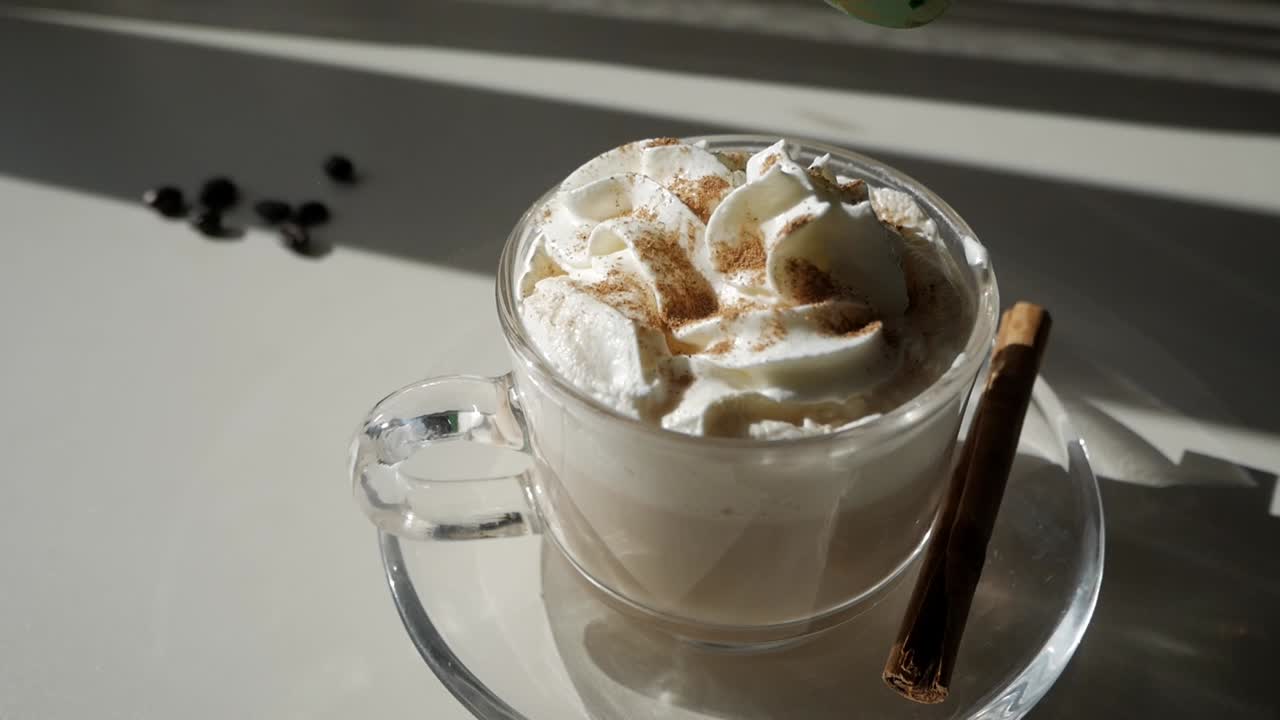 Close-up of pumpkin spice latte topped with whipped cream and cinnamon stick on white background under sunlight