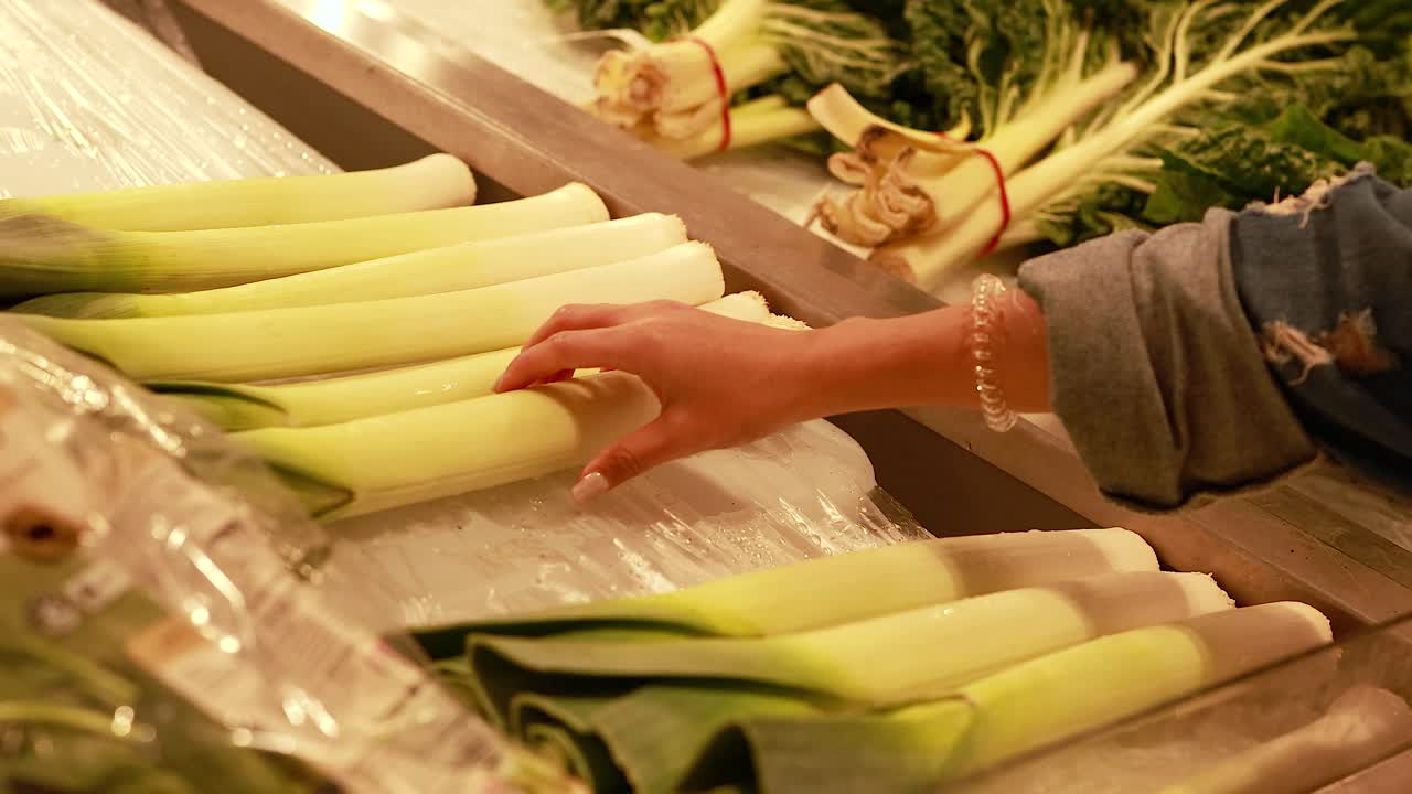 A person examines leeks under warm lighting in a Gold Coast supermarket, highlighting fresh produce selection