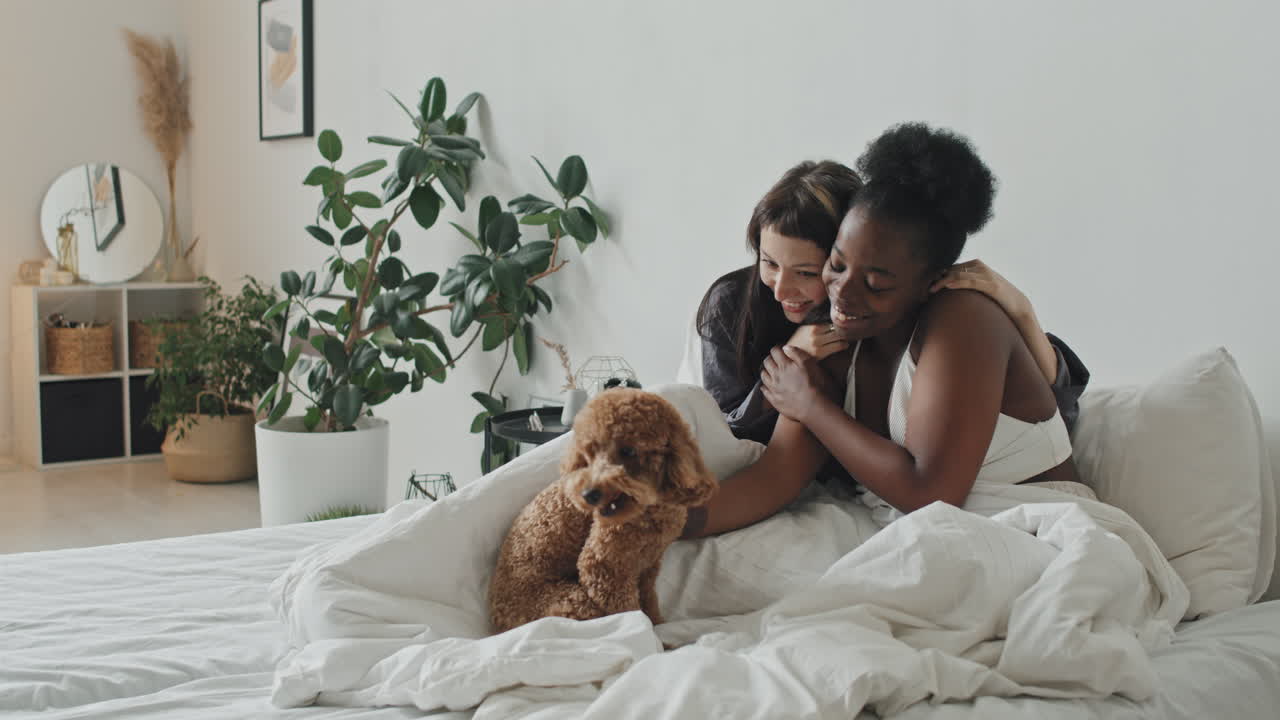 Felice coppia femminile che accarezza il proprio cane a letto