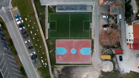 Alto-Vuelo-De-Drones-A-Vista-De-Pájaro-Sobre-Un-Pequeño-Campo-De-Fútbol-Junto-A-Un-Campo-De-Baloncesto-Donde-Se-Juega-Un-Partido