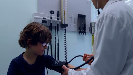 Side-view-of-young-asian-male-doctor-checking-blood-pressure-of-caucasian-boy-patient-in-clinic-4k