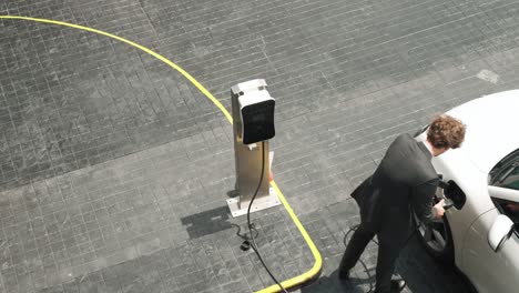 el hombre de negocios conecta el enchufe del cargador progresivo de la estación de carga a su ev.