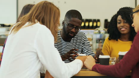 multiethnic group of friends talking while drinking coffe sitting at a table in a cafe