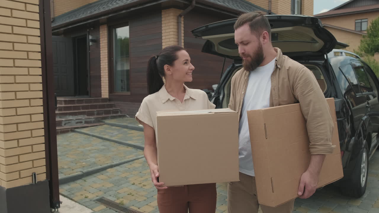 pareja feliz con cajas posando delante de la nueva casa