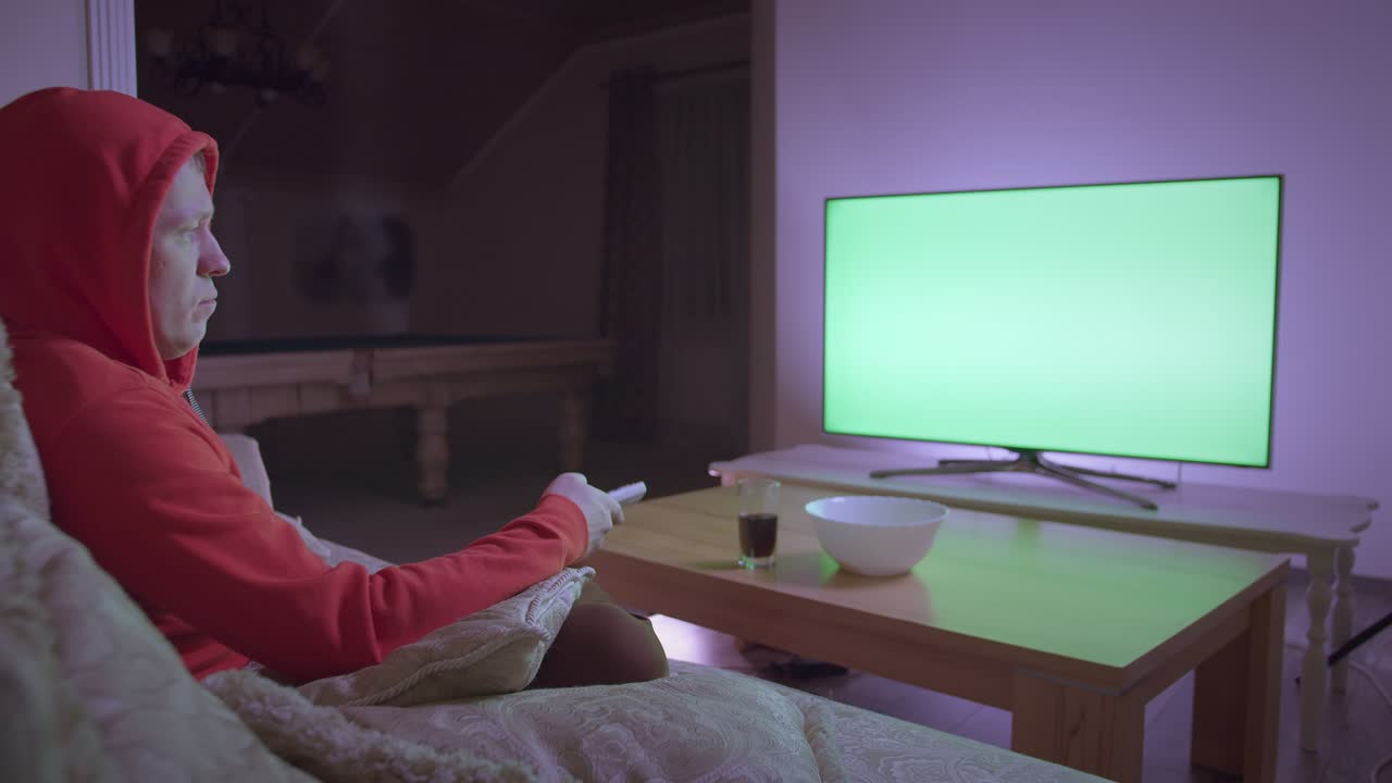 Mand i hættetrøje ser tv, sidder i sofaen derhjemme om aftenen, chromakey