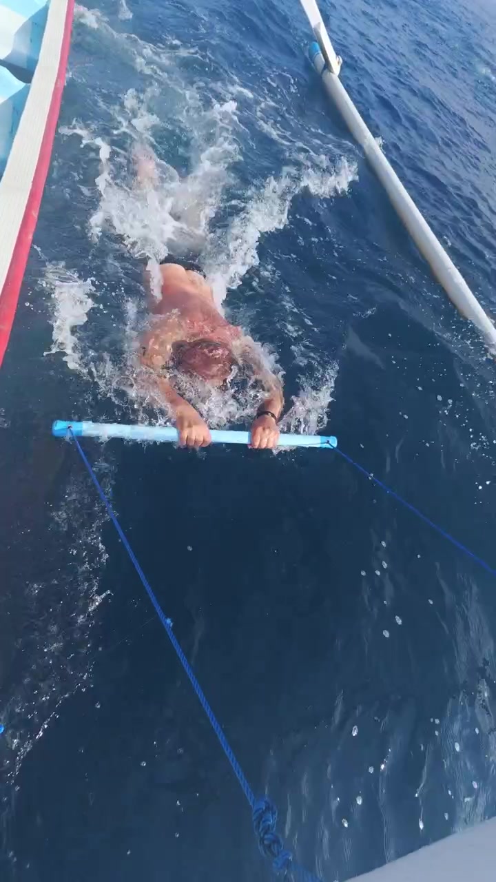 Spiaggia di Kelingking, Nusa Penida, Bali, Indonesia, snorkelista che tiene una tavoletta galleggiante accanto a una barca turistica nell'oceano blu profondo.