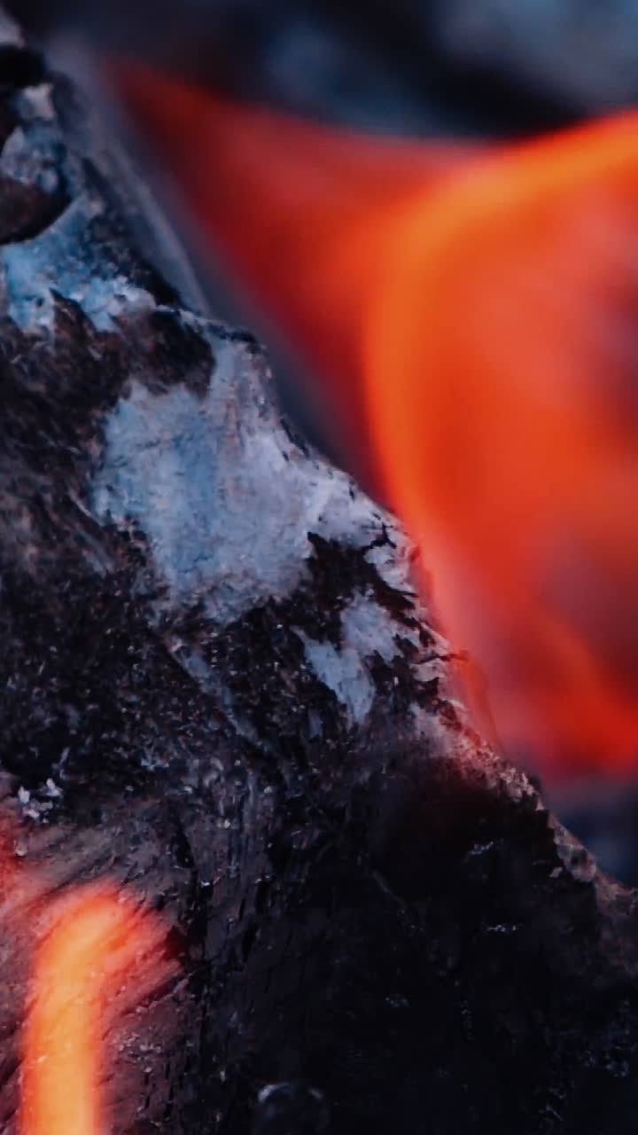 Wood burning with ash. Close-up shot of wood and charcoal with slight orange flame. Slow motion. Vertical video