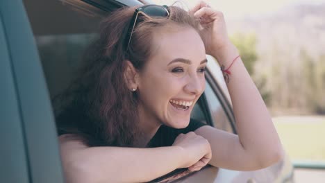 una mujer bonita se inclina hacia fuera del coche y saluda a un amigo en las tierras de cultivo