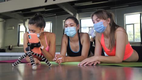 women friends exercising and taking online class in a gym, wearing masks.