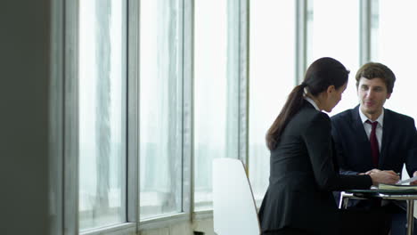 three coworkers meeting, sitting at a table, while discussing details of a project