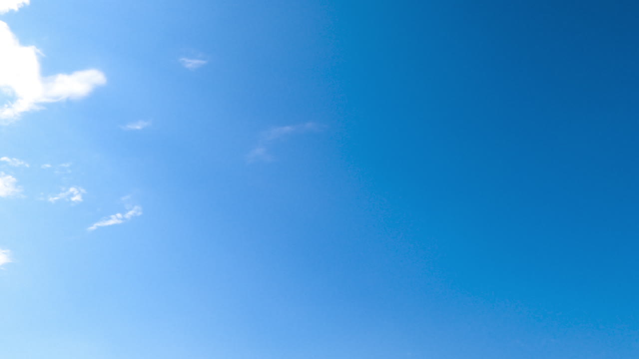 Blue sunny sky clears up from white clouds. Light spindrift clouds flying quickly by the horizon disappearing from sight.