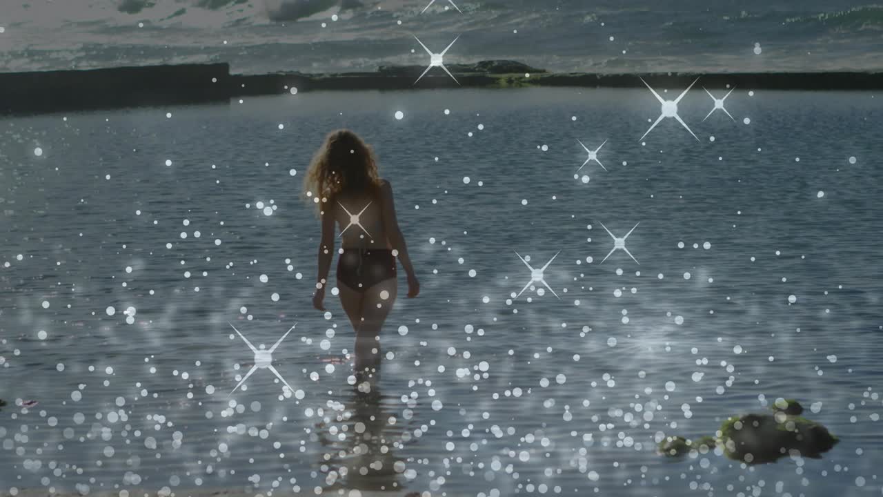 Frau geht ins Meer, erzeugt beim Treten Wellenringe, während ein Funkel-Overlay glitzernd über ihren Weg gleitet.
