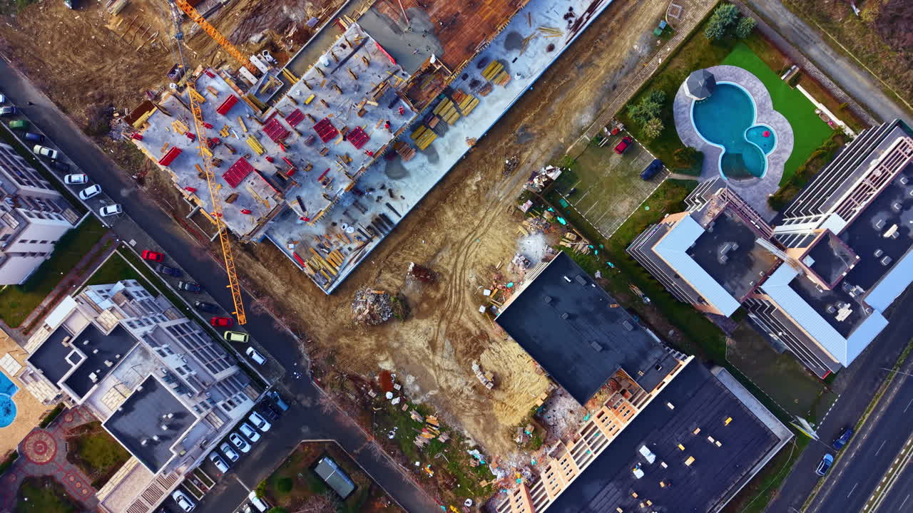 Construction site in urban area with buildings, roads, and swimming pool visible from above during daylight hours