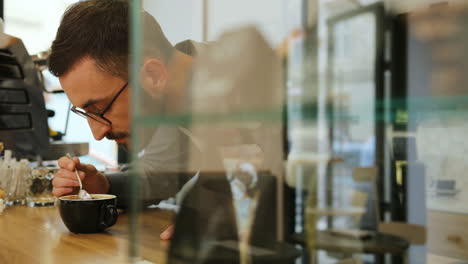 vista lateral del barista masculino caucásico con barba y gafas olfateando el café recién hecho en una cafetería