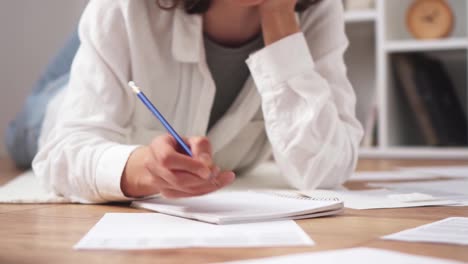 la estudiante se acuesta, se sienta en el suelo, escribe, llena documentos de papel. la chica se sienta en el suelo