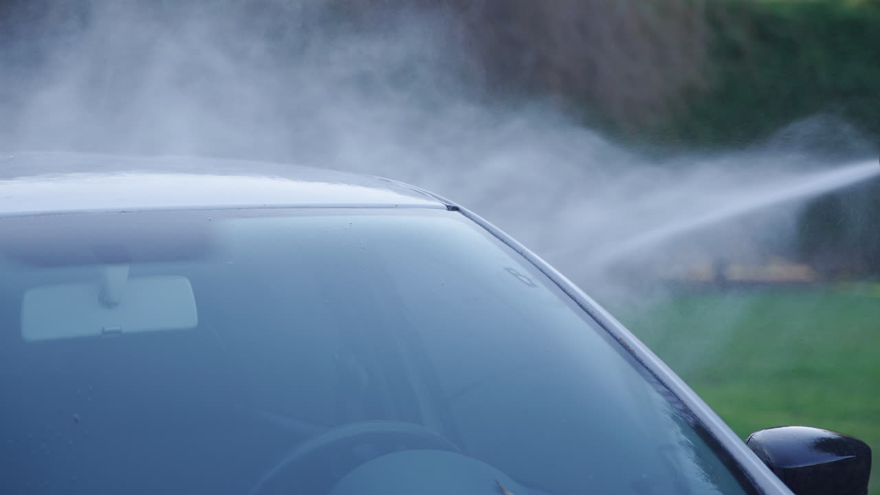 高壓水柱正在清洗一輛白色汽車的擋風玻璃。