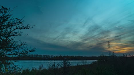 Sun-setting-down-near-river-Scheldt-making-colorful-sky-with-traces-of-planes-flying,-time-lapse