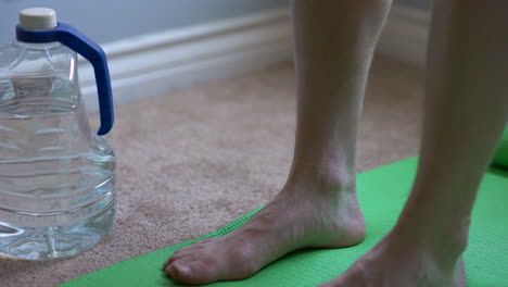 close up shot of an at home work out plus a green yoga mat, yoga mat strap, and water bottle