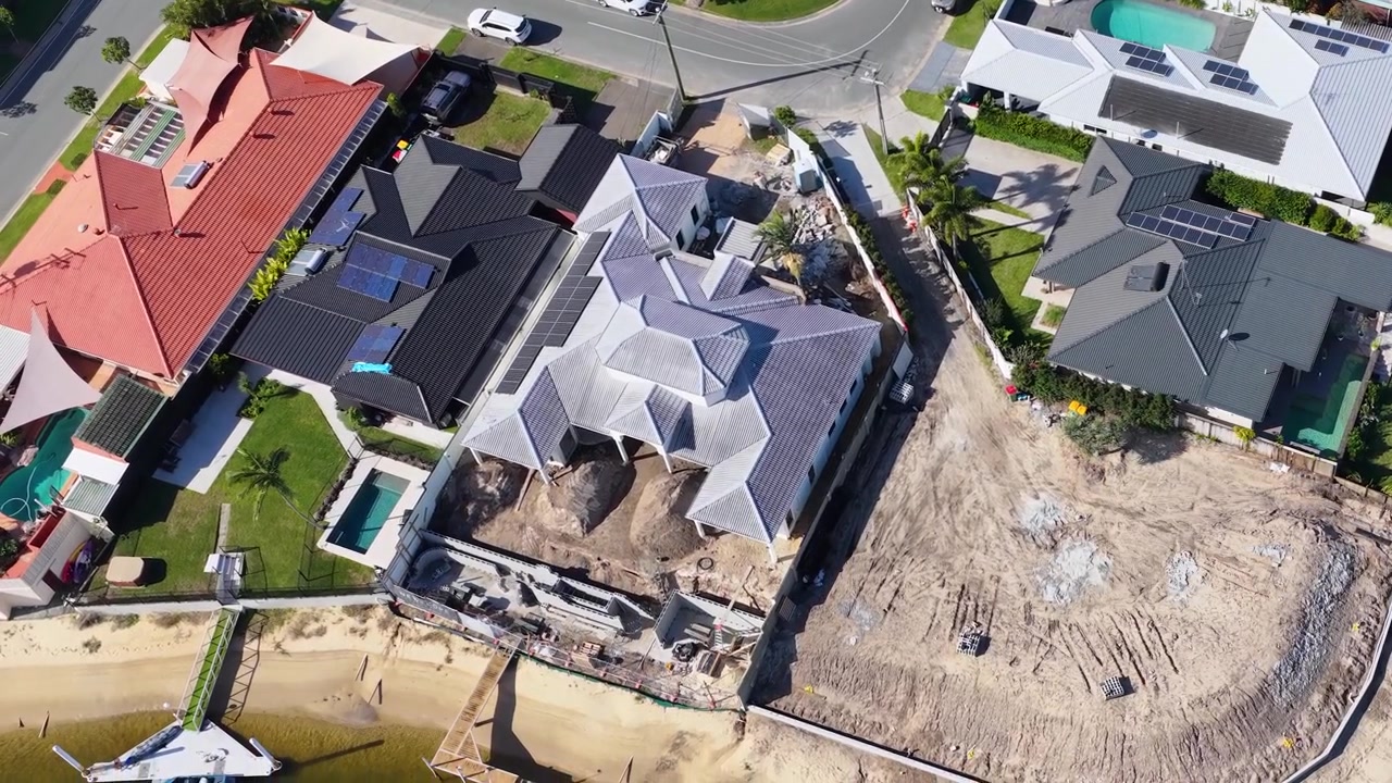 High-angle drone shot reveals residential construction progress beside a canal under bright daylight.