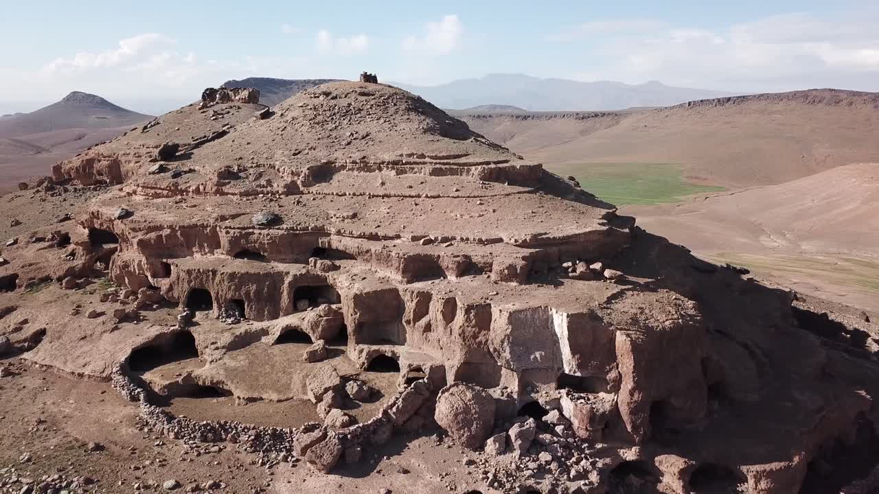 Aerial drone shot of a high mountain peak in the High Atlas. Highlights include natural geological caves, weathered rock formations, and arid cliff textures in the Moroccan mountains