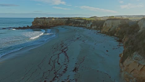 Aerial-reveal-of-secluded-sandy-bay-with-gentle-rolling-waves-at-Mitchells-Rocks-in-Otago,-South-Island-of-New-Zealand-Aotearoa