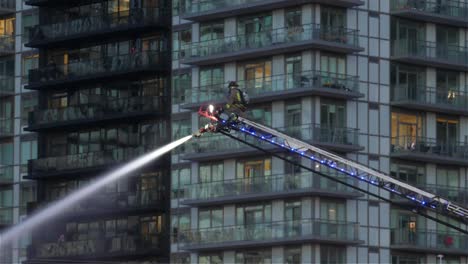 solo firefighter in action, fighting the fire on top of the aerial hydraulic ladder apparatus in an urban skyscraper environment